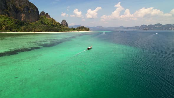 wide aerial of a thai longtail boat motoring in the turquoise blue Andaman sea surrounded by coral r