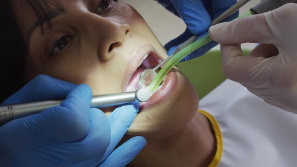 Hands of male dentist with dental nurse examining teeth of female patient at modern dental clinic