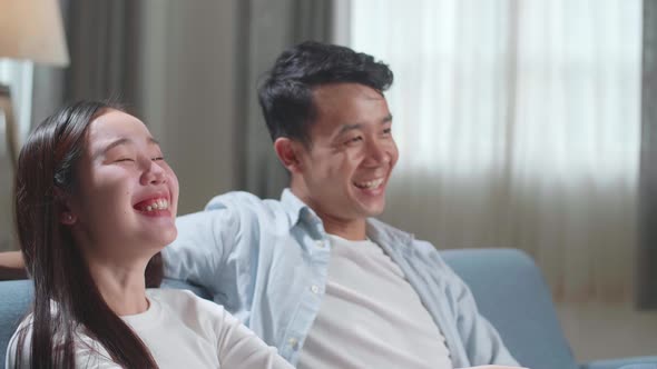 Happy Young Asian Couple Relaxing And Watching Tv At Home