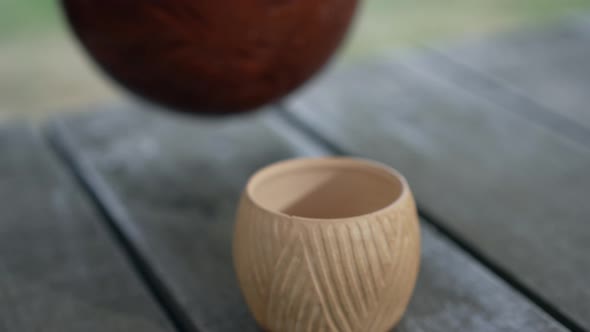 Closeup Clay Cup with White Milk Pouring From Pot in Slow Motion