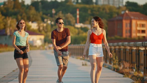 Young Friends Riding Skateboards on a Quay on a Background of Modern Buildings - Orange Sunset