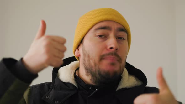 Portrait of Young Bearded Man in Winter Clothes Showing Thumbs Up and Looking at Camera