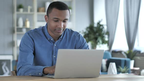 Pensive Young African Man Thinking and Working on Laptop