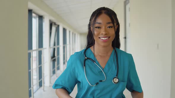 Young African American Female Doctor in a Blue Suit and with a Stethoscope Stands in the Corridor of