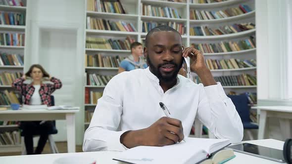 African American Guy which Making Notes Into Copybook During His Phone Conversation alt