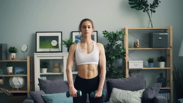 Strong Young Woman in Sportswear Doing Exercises with Dumbbells in Apartment