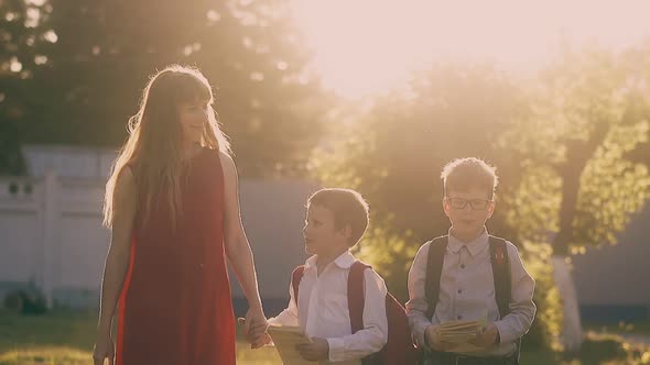 Lady in Red Dress Walks Holding Children with School Bags