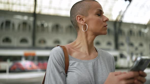 Smiling bald woman wearing t-shirt typing by phone and looking around