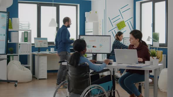 African Paralysed Woman in Wheelchair and Colleague Analyzing Reports Laptop