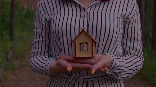 Close Up of Body Part of Woman with Small Wooden House in Hands Standing in Forest