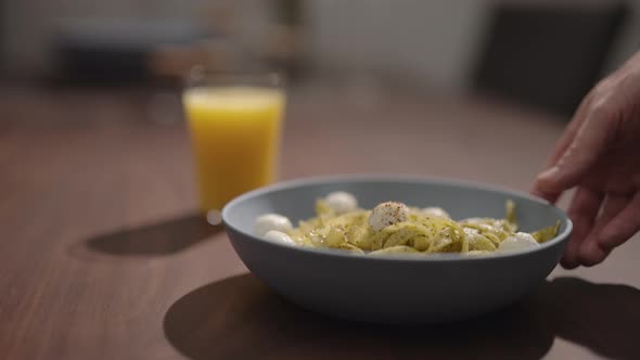 Slow Motion Man Put Pesto Fettuccine with Mozzarella in Blue Bowl on Walnut Table