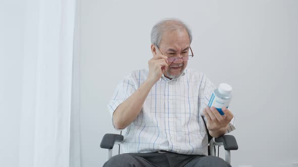 Asian senior male sit on wheelchair and read prescription of medicine.