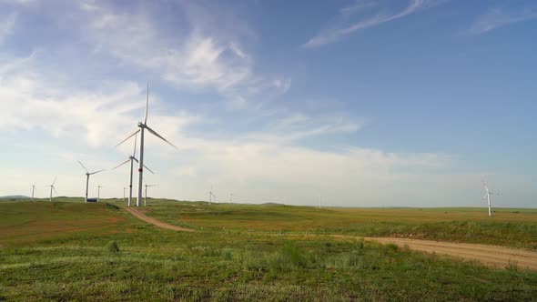 Motion the Blades of a Large Wind Turbine in a Field Against a Background of Cloudy Blue Sky Near