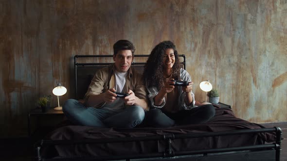 Excited Man and Woman in Casual Outfit are Laughing Holding Wireless Gamepads and Playing Video Game