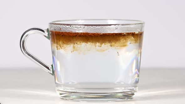 Preparing instant coffee with hot water in glass cup over white