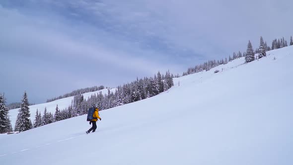 Tourist with a Backpack Climbs the Snowy Slope