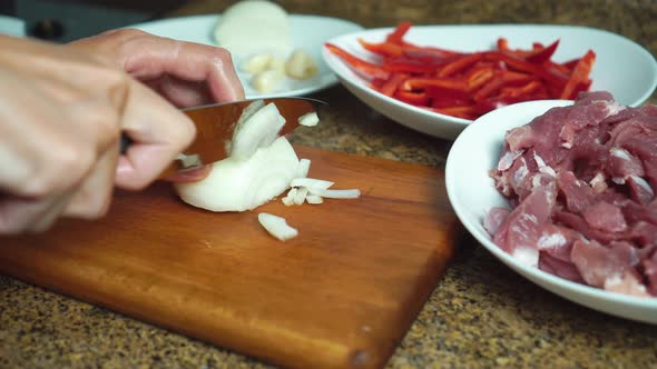 woman uses kitchen knife to slice onions on chopping board.