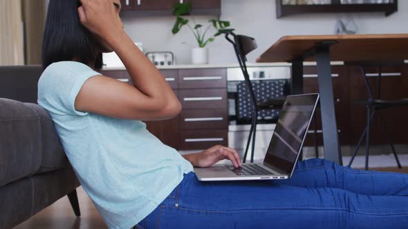 Mixed race gender fluid person sitting on floor and using laptop at home