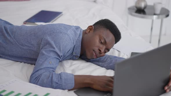 African American Young Businessman Falling Asleep Lying on Bed with Laptop