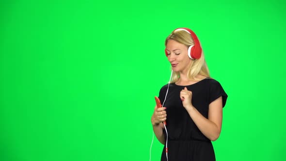 Blonde Girl Walks in Big Red Headphones and with a Smartphone, Switches Music and Dancing. Chroma
