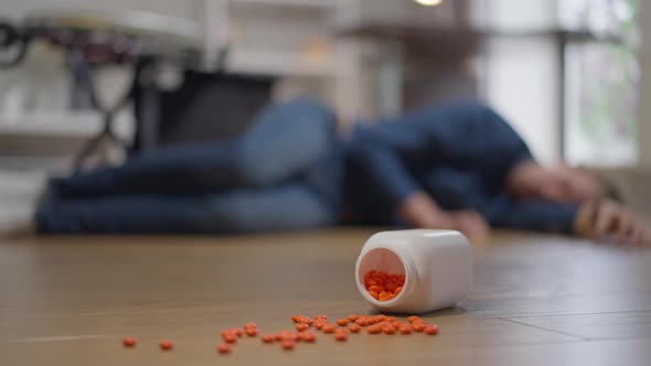 Closeup Pills Fallen on Floor with Blurred Disabled Man Lying at Background with Wheelchair Rolled