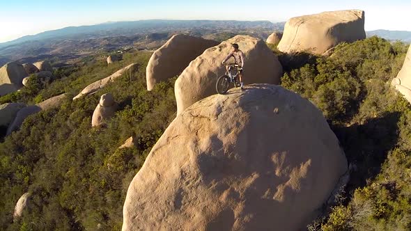 Aerial shot of young man mountain biker resting with his bike on a boulder.