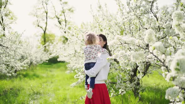 Mom Spinning with a Daughter in Her Arms in the Park By a Flowering Tree