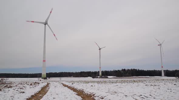Low angle shot of rotating wind turbines on a snowy field in Germany. Wide shot of a wind farm.