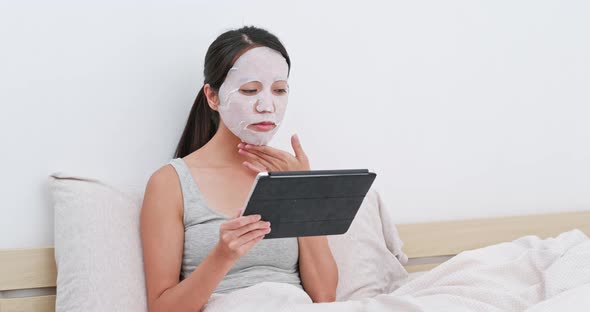 Woman apply facial mask and watching on tablet at home