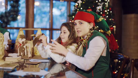 An Elf in a Green Suit is Sitting at the Table and Talking About the Letters for the New Year