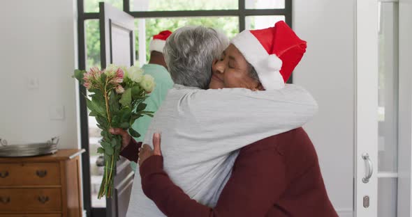 Two diverse senior female friends welcoming in doorway at christmas time