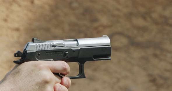 Slow motion of a man firing a hand gun in a firing range with cartridge flying away