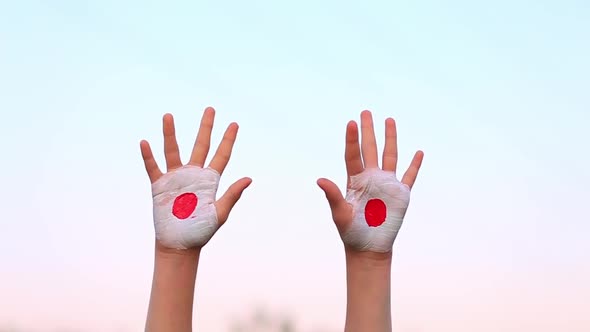 Child Hands Painted in Japan Flag Colors Making Different Signs Outdoor Over Sky Background