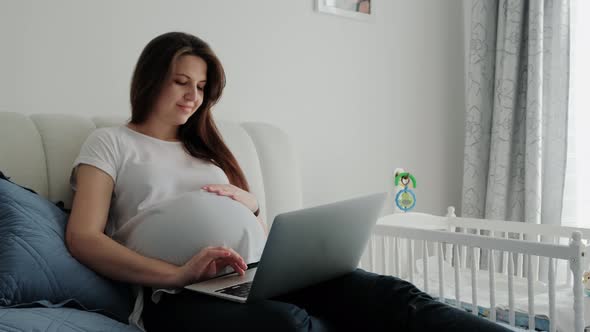 Pregnant Woman Resting on a Sofa at Home and Working with Laptop Computer Using Online Technology