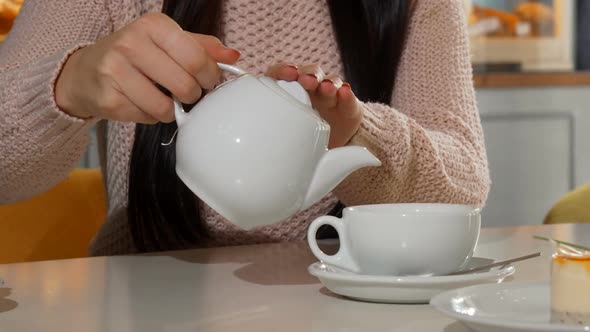 Woman Pouring Aromatic Tea Into Her Cup at the Coffee Shop