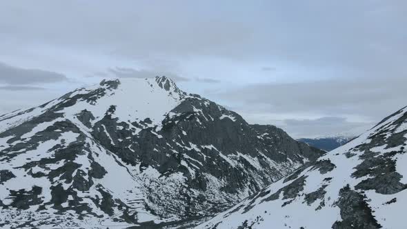 Aerial Drone Eis Fly Above Dark Snowy Mountains in Frozen Lake Isoba, cloudy sky in cold elevations