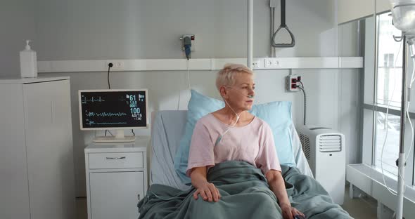 Ill Mature Woman with Nasal Cannula Sitting in Hospital Bed