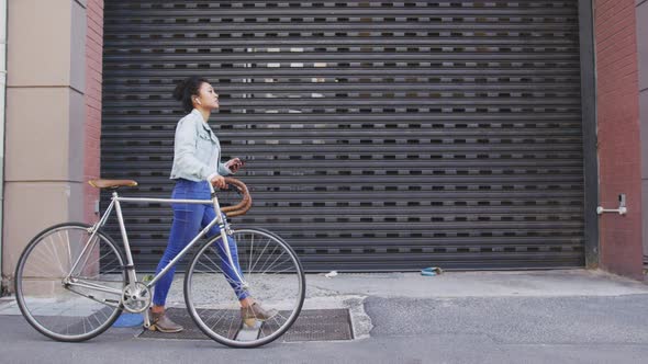 Mixed race woman walking next to her bike on the street
