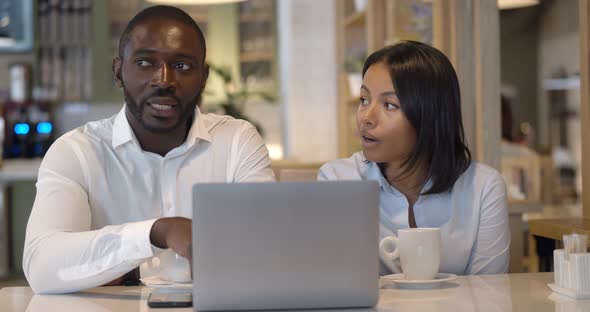 Mixed Race Young Couple of Colleagues Working on Laptop Computer While Sitting at Cafe