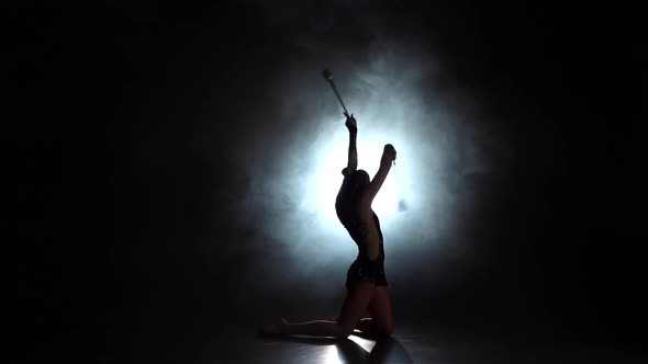 Rhythmic Gymnast Throws Mace Up and Catches Her. Black Background. Light Rear. Silhouette. Slow