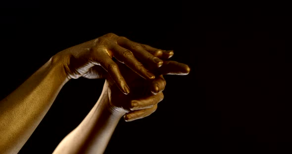 Close-up of Female Hands with Golden Glowing Skin on a Black Background. Fingers Intertwine