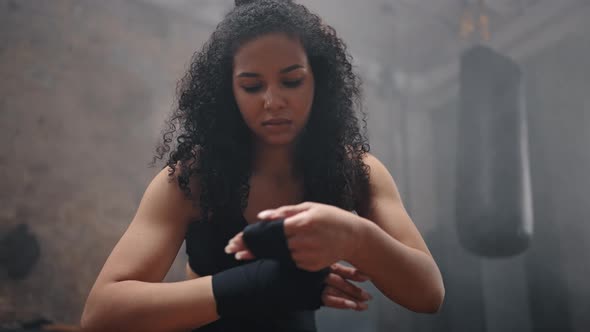 Young Woman with Dark Kinky Hair Wraps Hand for Boxing