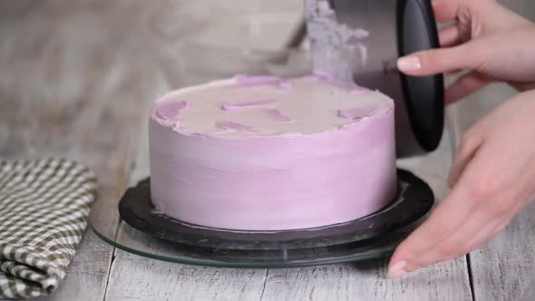 The process of decorating a cake with purple cream cover. 