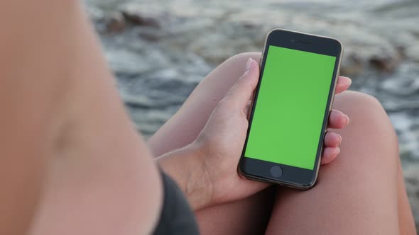 NICE, FRANCE - JULY 2017 Female holding  green screen display smart phone on wavy beach