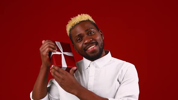 Latin Hispanic Man in White Tshirt in Red Studio Background with Small Gifts Box