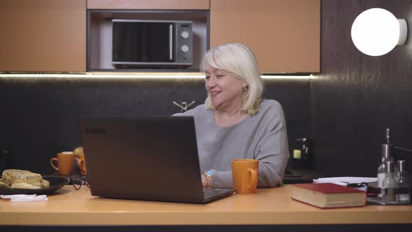 Carefree Senior Woman Opening Laptop and Putting on Eyeglasses. Portrait of Relaxed Beautiful