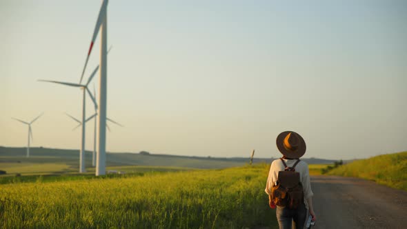 Young woman with a retro camera near the road with a field with alternative energy turbines