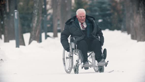 An Old Man Veteran Sitting in a Wheelchair Under the Snowfall