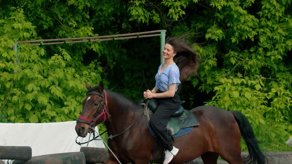 Young Smiling Happy Woman with Long Hair in Blue Shirt Riding a Horse