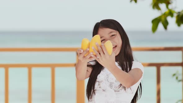 A Charming Philippine Schoolgirl Girl in a White Dress and Long Hair Positively Poses with a Mango